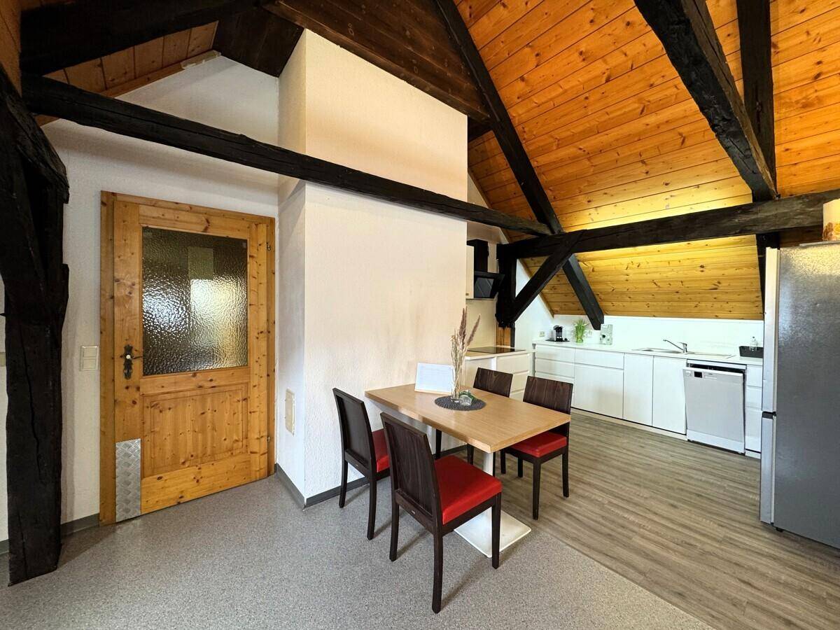 Essbereich mit Holztisch und Stühlen, angrenzend an die moderne, weiße Einbauküche.