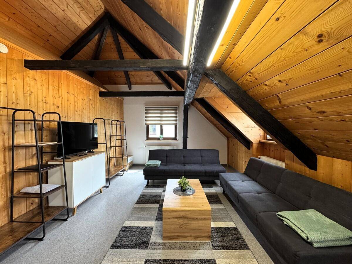 Heller Wohnbereich mit bequemen Sofas, Holzdachschrägen und einem Fernseher.