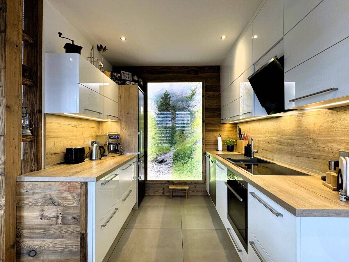 Helle moderne Küche mit weißen Hochglanzschränken, Holzakzenten und Fensterblick.