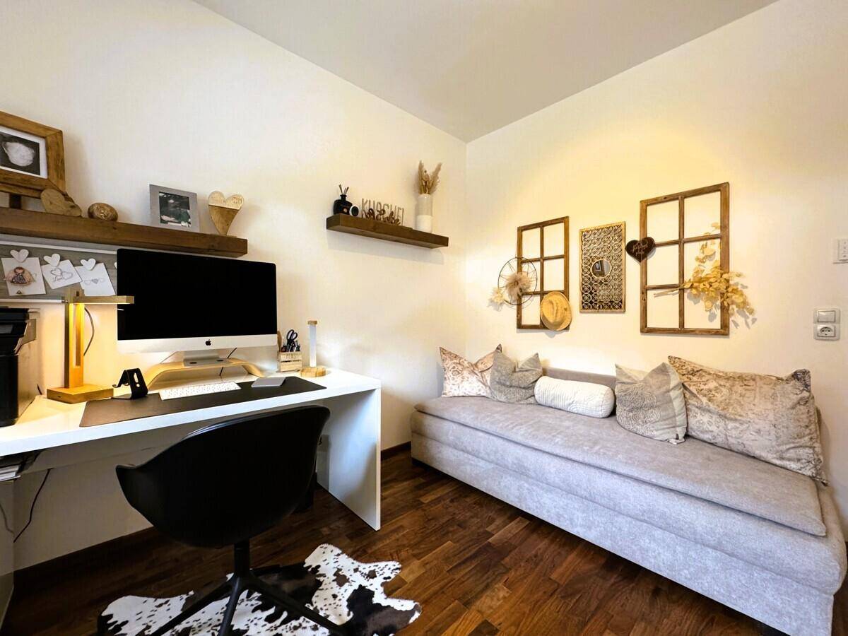Helles Arbeitszimmer mit Schreibtisch, Sofa und rustikalen Dekorationselementen.