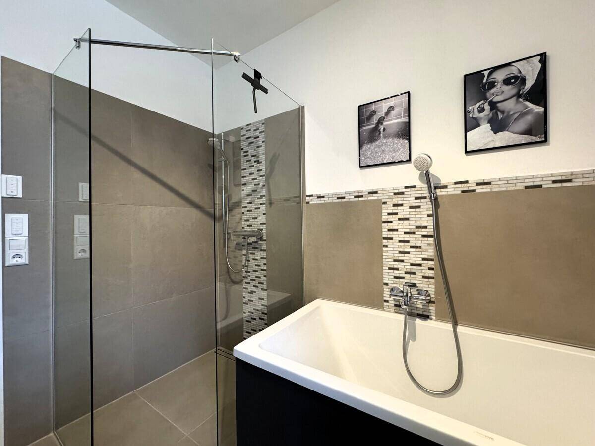 Helles Badezimmer mit Badewanne, Glasdusche und modernen Fliesen.