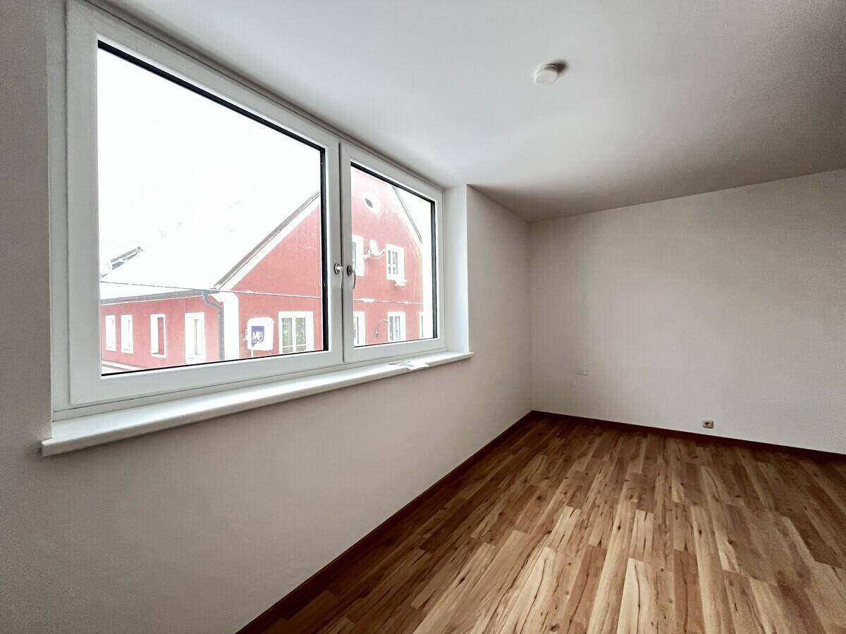 Helles Schlafzimmer mit großem Fenster und Blick auf die umliegenden Gebäude.