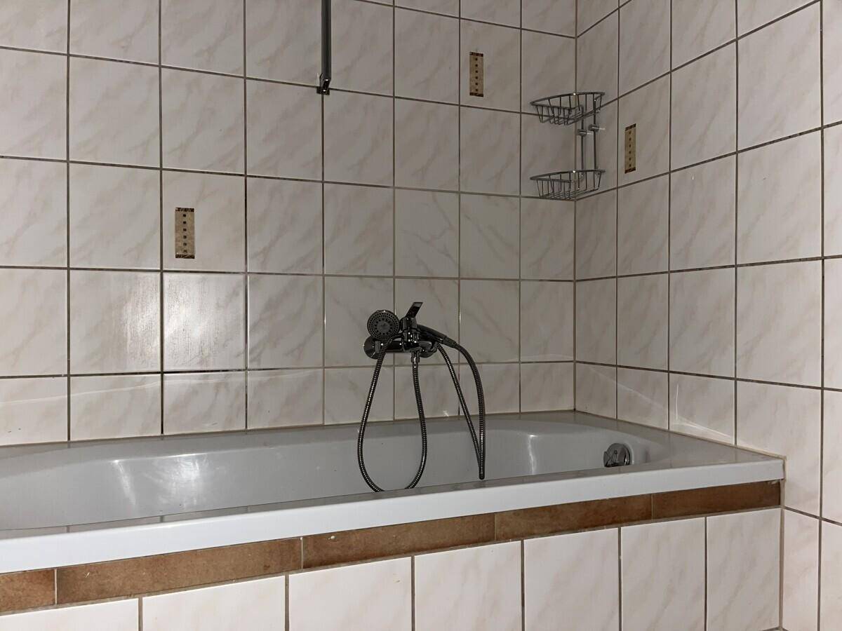 Badezimmer mit Badewanne und hellen Fliesen, ausgestattet mit einer Duscharmatur.