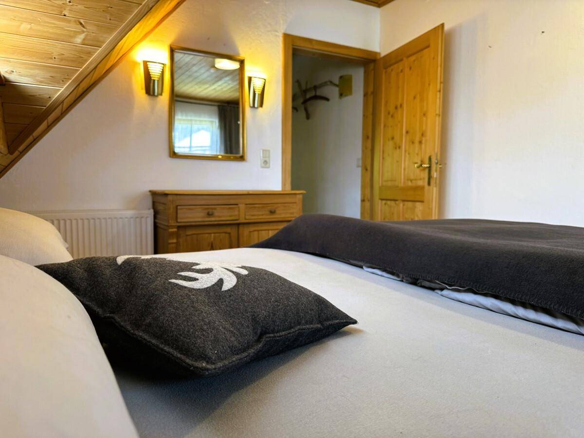 Gemütliches Schlafzimmer im Dachgeschoss mit Holzbalkendecke, Holztüren und einem Spiegel über der Kommode.
