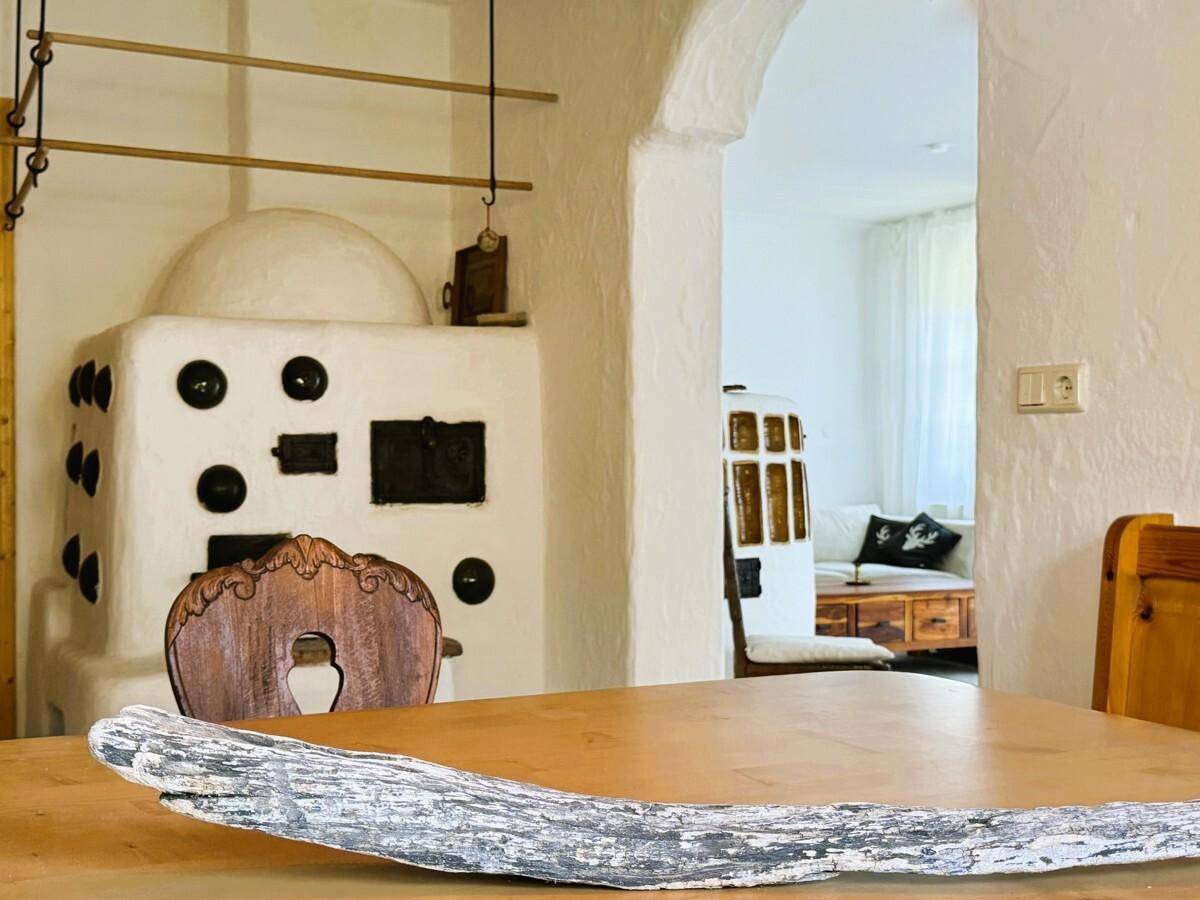 Kachelofen im Essbereich mit Blick durch einen Bogen in das helle Wohnzimmer.