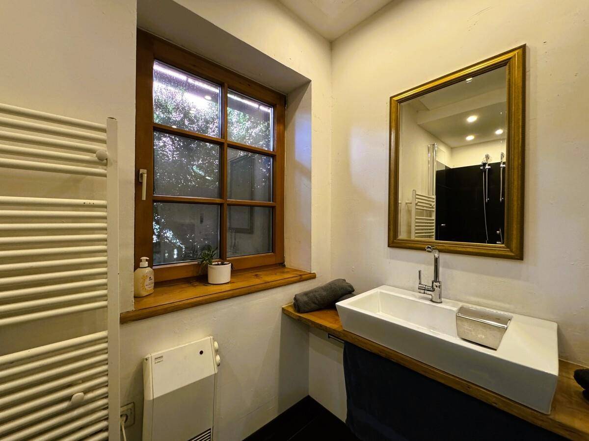 Modernes Badezimmer mit Fenster, Einzelwaschbecken auf Holzplatte und beheiztem Handtuchhalter.