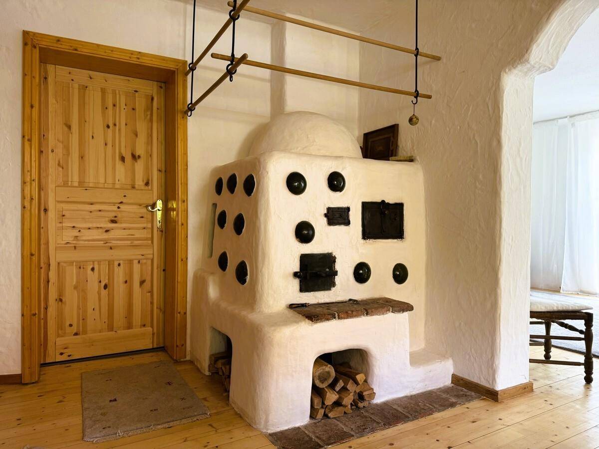 Traditioneller Kachelofen mit Holzscheiten und rustikaler Holztür im Essbereich.