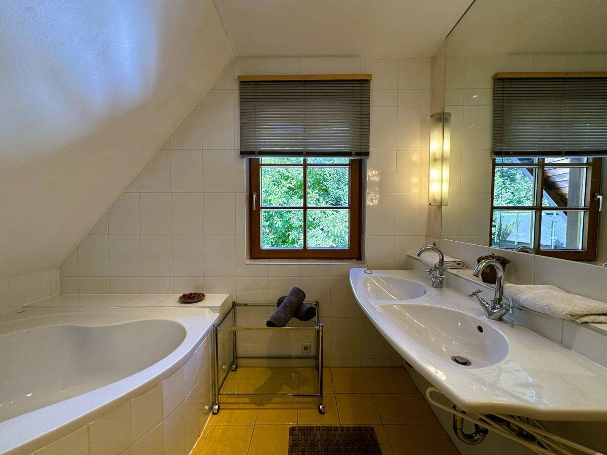 Helles Badezimmer im Dachgeschoss mit Badewanne, Doppelwaschbecken und Fenster mit Blick ins Grüne.