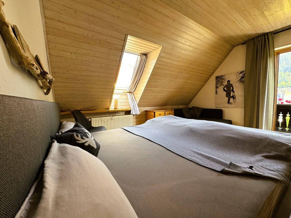 Geräumiges Schlafzimmer im Dachgeschoss mit Holzbalkendecke, Dachfenster und Bergblick.