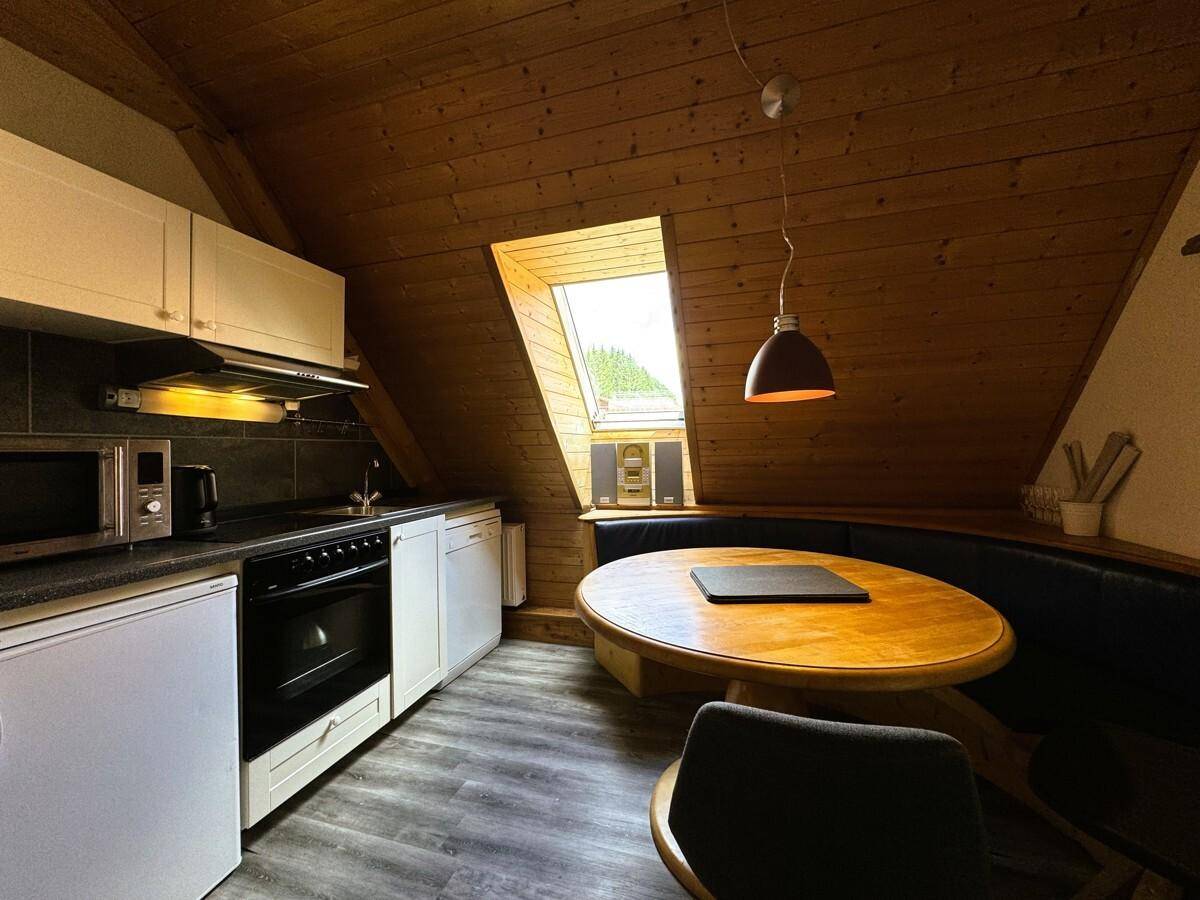 Kleine Küche im Dachgeschoss mit Holzbalkendecke, Dachfenster und einer gemütlichen Essecke.