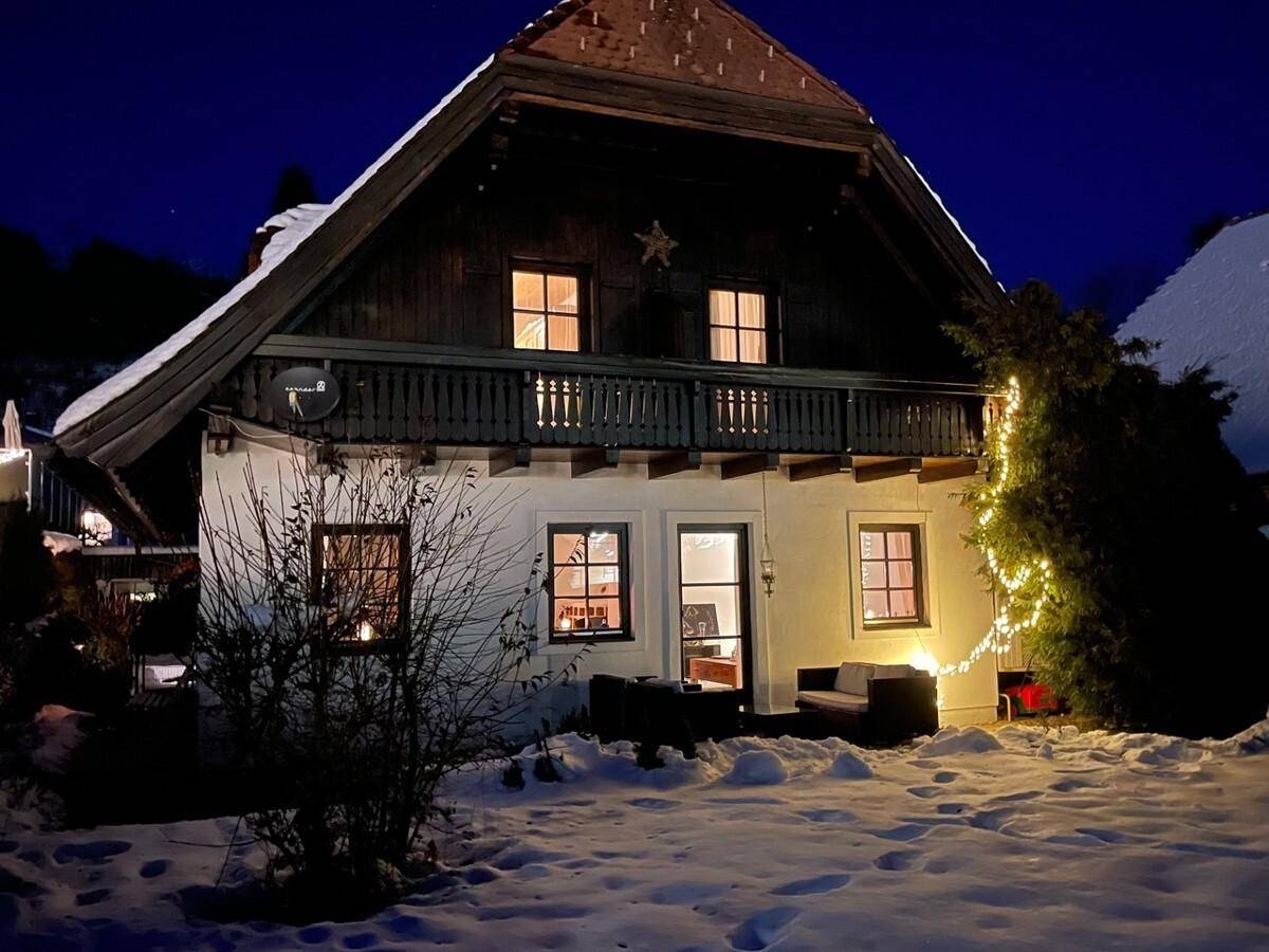 Winterliche Ansicht des Hauses bei Nacht mit Schnee und festlicher Beleuchtung im Garten.