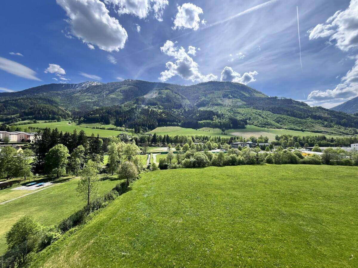 Weitläufiger Panoramablick auf die grüne Berglandschaft und weite Felder unter strahlend blauem Himmel.
