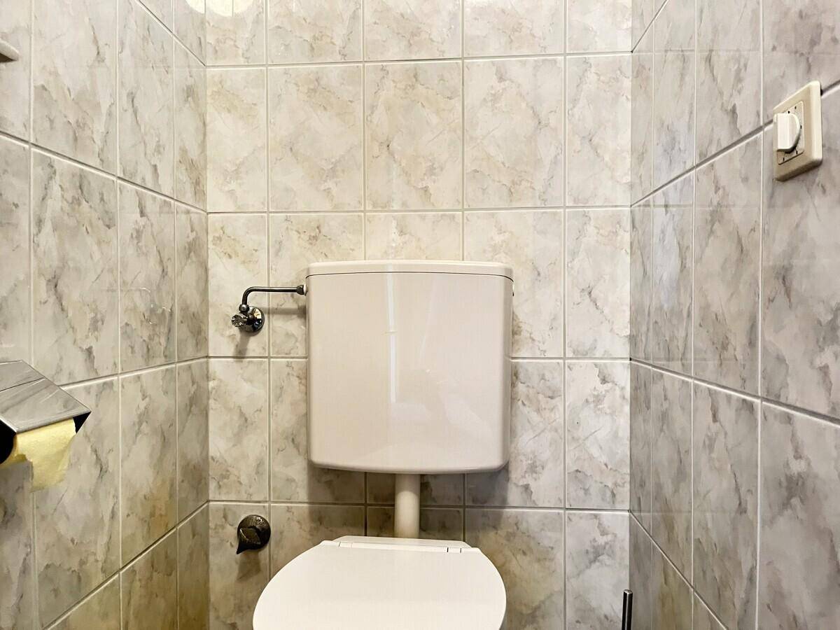 Kleines WC mit hellgrauen Fliesen an Wänden und Boden, ausgestattet mit einer Toilette.