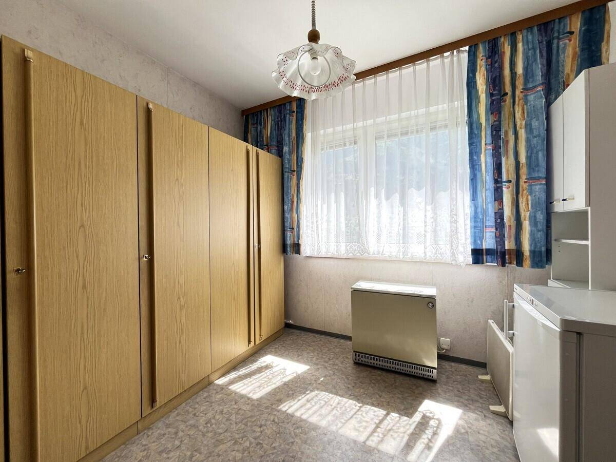 Helles Zimmer mit großen Holzschränken, Fenster mit bunten Vorhängen und gemustertem Boden.