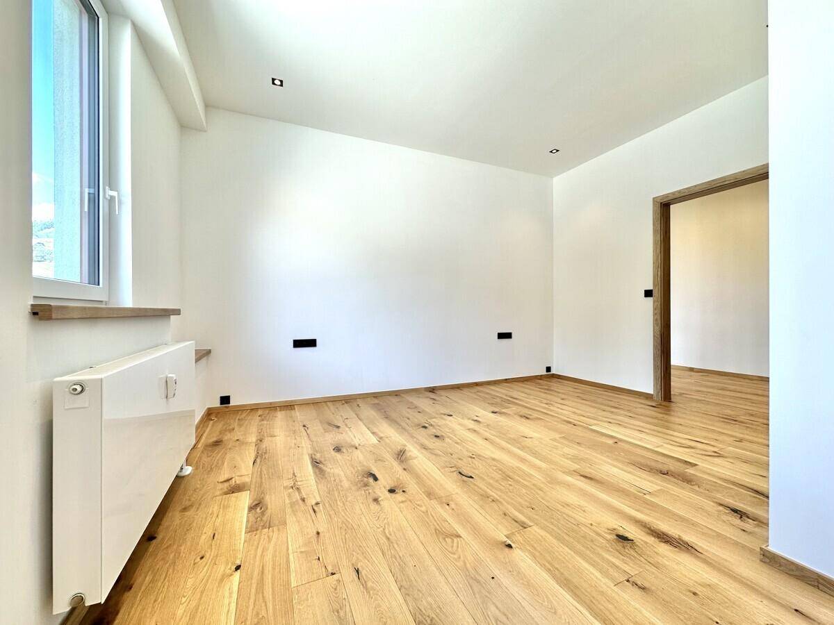 Leerer Wohnraum mit Holzboden, weiß gestrichenen Wänden und einem Fenster.