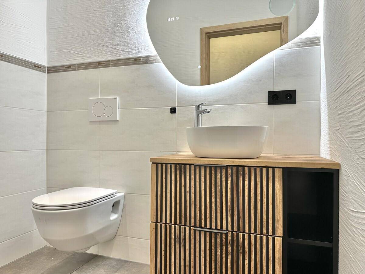 Modernes Gäste-WC mit Wand-WC, Einzelwaschbecken und beleuchtetem Spiegel.