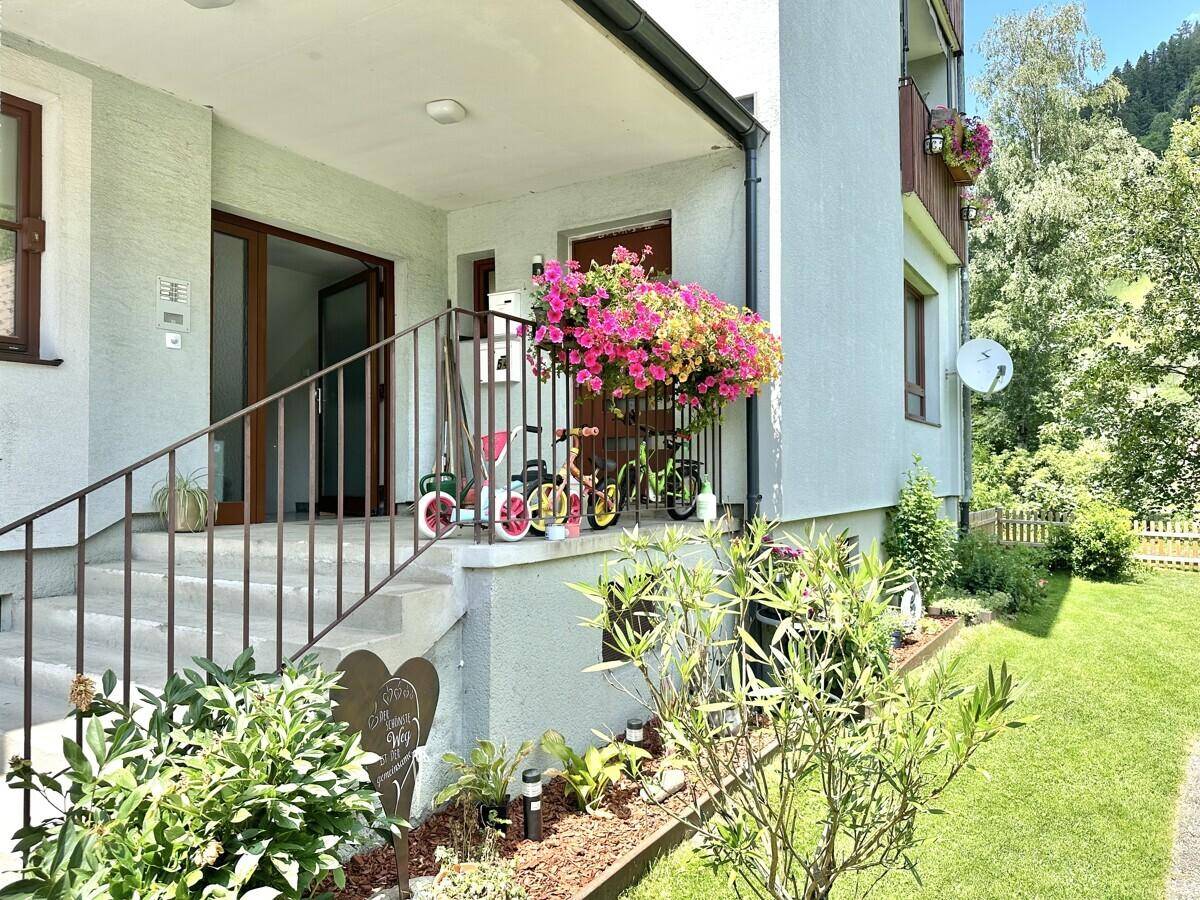Eingangsbereich eines Mehrfamilienhauses mit Treppe, Blumen und Garten.