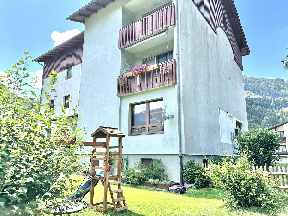 Gartenbereich eines Mehrfamilienhauses mit Rasenfläche, Spielturm und Balkonen.