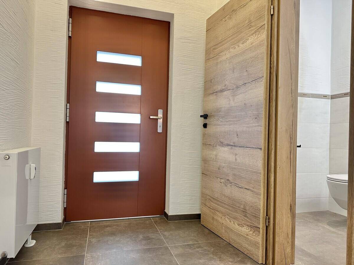 Eingangsbereich mit brauner Haustür, Fliesenboden und Zugang zu einem Badezimmer.