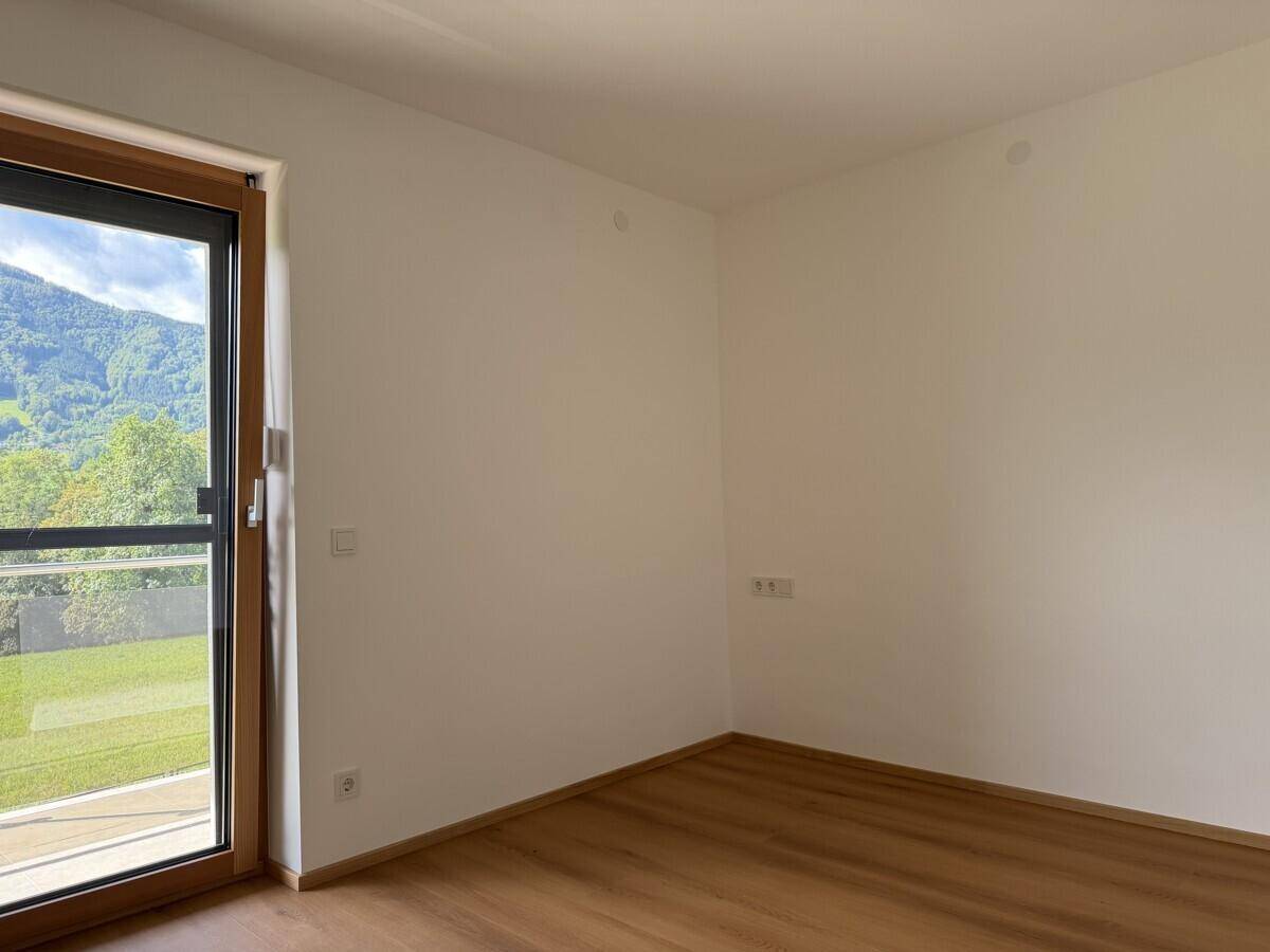 Leerer Raum mit Holzboden und Zugang zu einem Außenbereich mit grüner Aussicht.