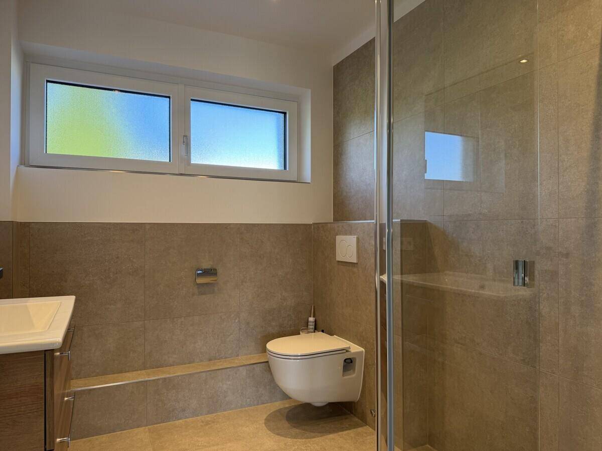 Modernes Badezimmer mit beigen Fliesen, wandhängendem WC und einer begehbaren Dusche.