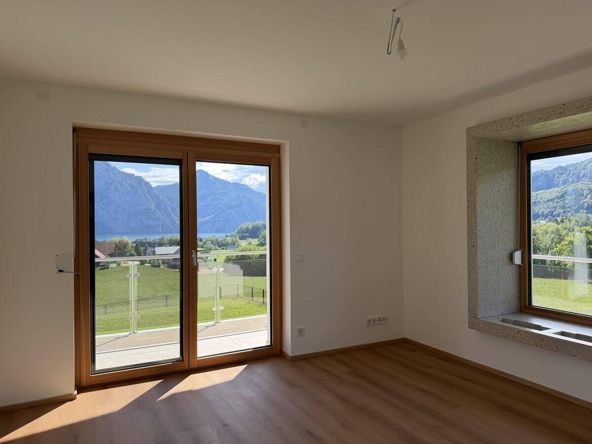 Heller Raum mit Holzboden, großem Balkonzugang und weitem Berg- und Seeblick.
