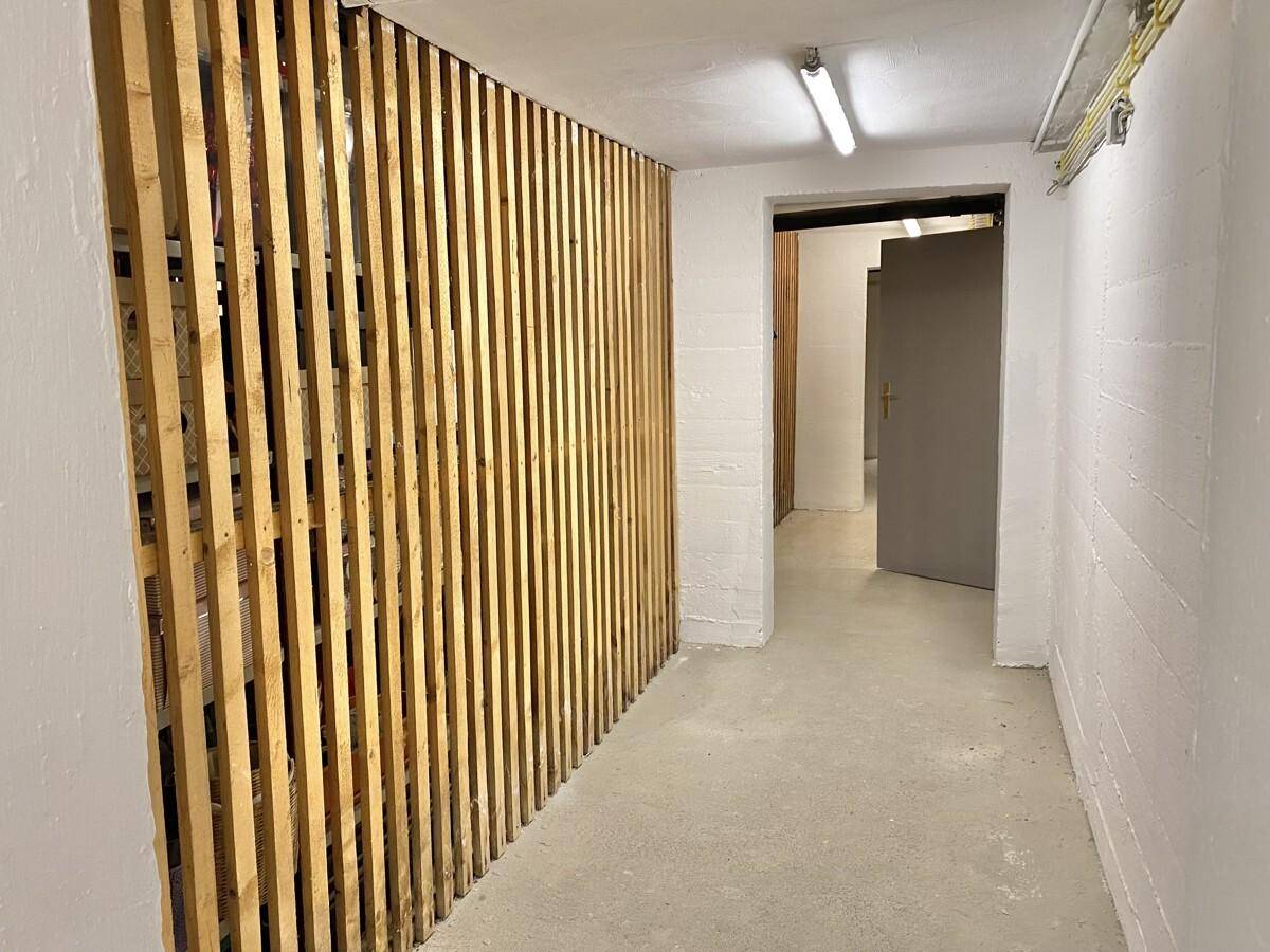 Kellerraum mit Holzlattenverschlägen und Betonboden, ideal als Abstellfläche.