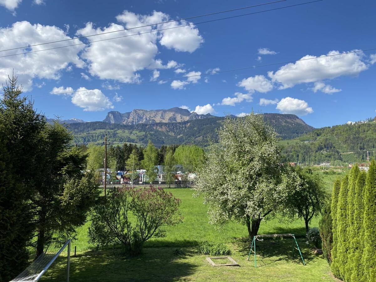 Grüner Gartenbereich mit Bäumen, Schaukel und weitem Blick auf die Berge.