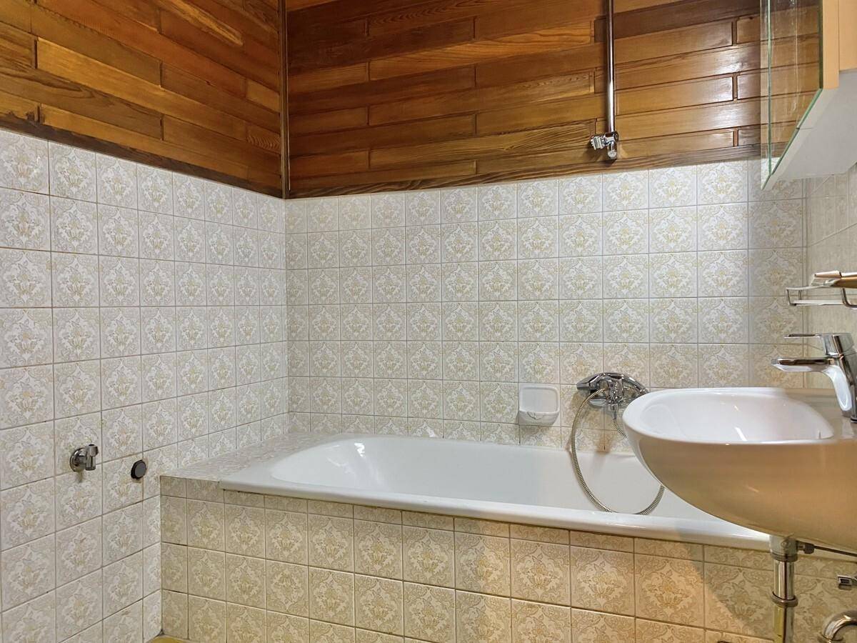 Badezimmer mit Badewanne, Waschbecken und gemusterten Fliesen sowie Holzverkleidung.