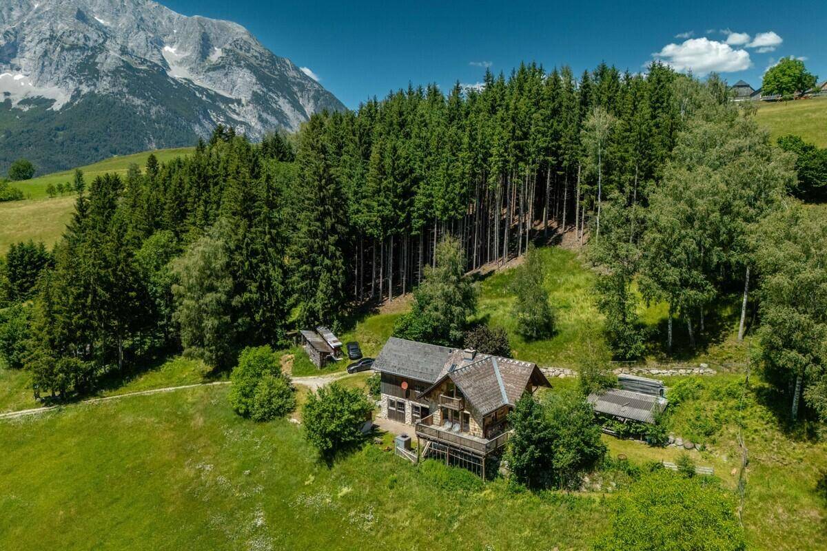 Idyllisches Holzhaus am Waldrand mit Blick auf die umliegende Berglandschaft und grüne Wiesen.