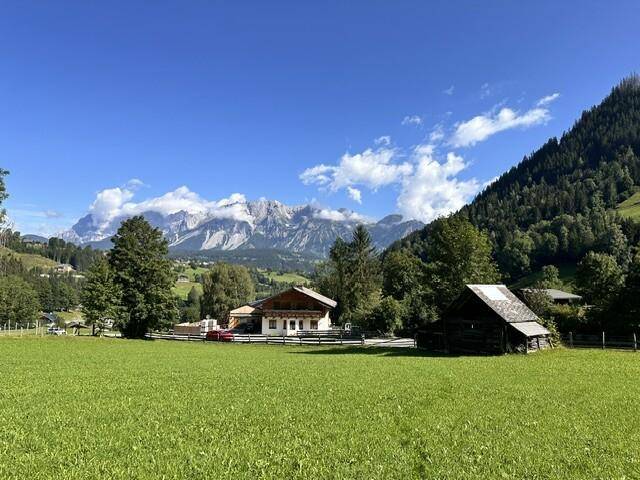 Traditionelles Haus und Scheune in einer idyllischen grünen Landschaft mit Bergblick.