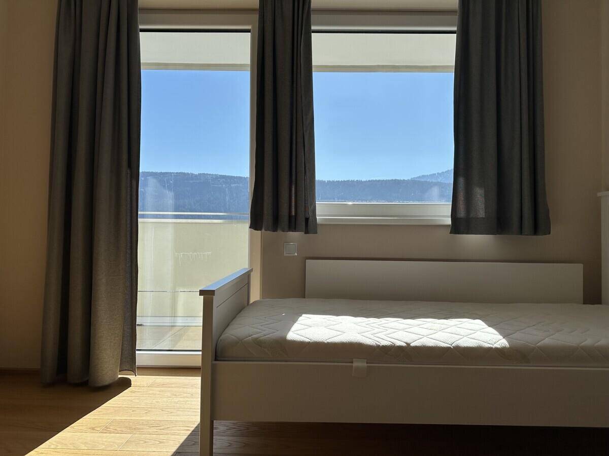 Helles Schlafzimmer mit Einzelbett und Balkonzugang mit Bergblick.
