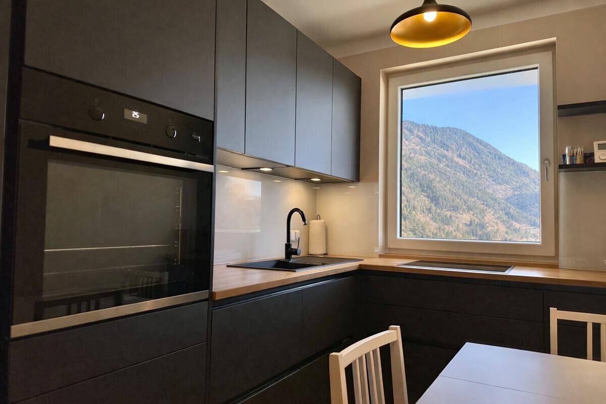 Moderne Küche mit dunklen Schränken, Holzarbeitsplatte und Essbereich mit Bergblick.