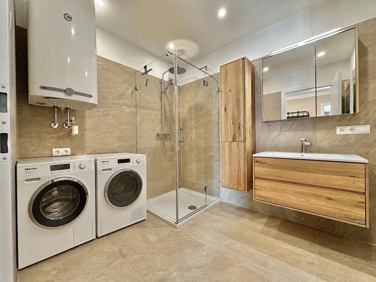 Modernes Badezimmer mit begehbarer Dusche, Holzwaschtisch und integrierter Waschmaschine und Trockner.