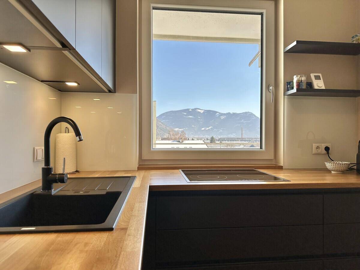 Küchenzeile mit Holzarbeitsplatte, Induktionskochfeld und Fenster mit Bergblick.