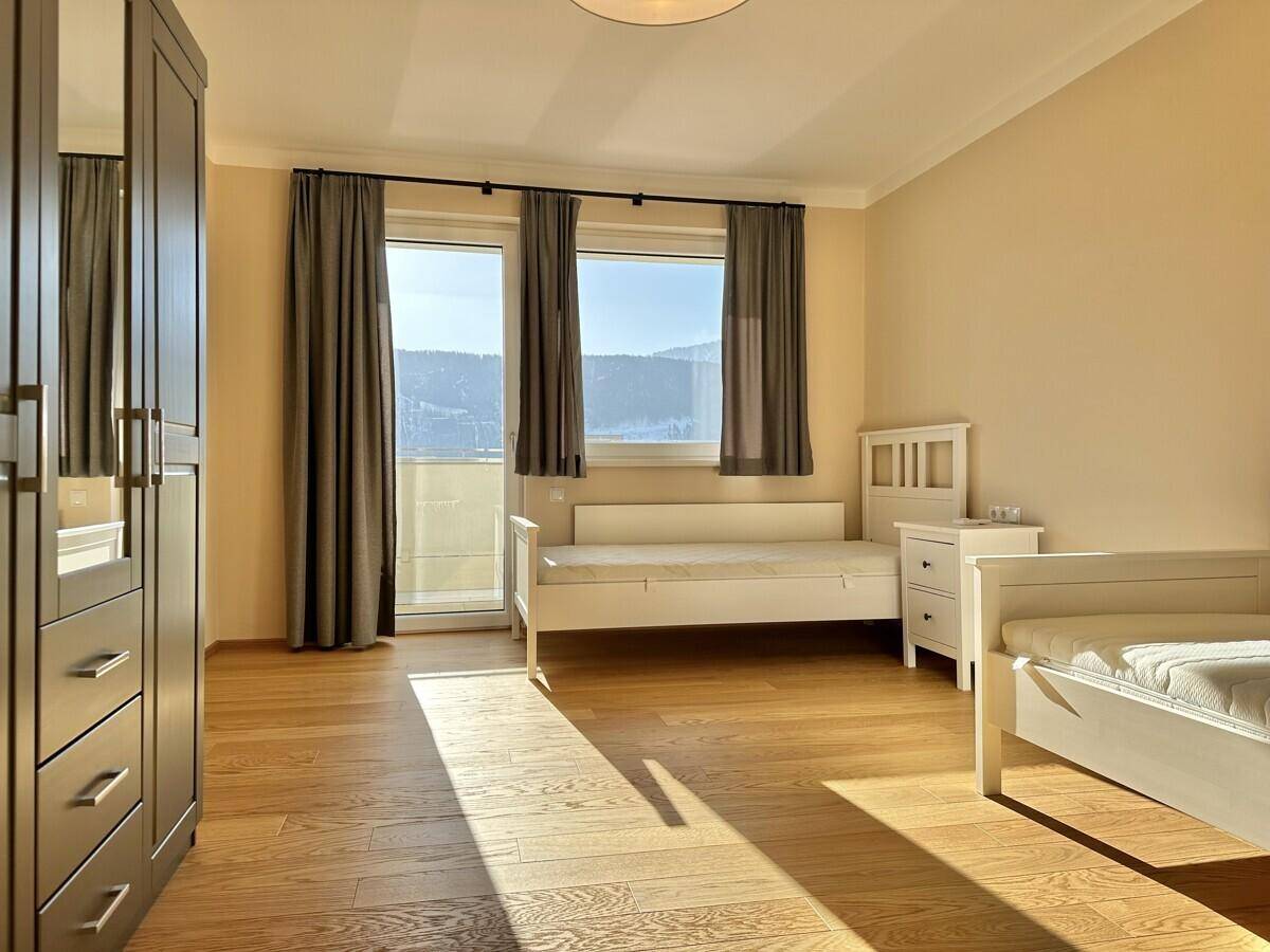 Helles Schlafzimmer mit zwei Einzelbetten, Kleiderschrank und Balkonzugang mit Bergblick.