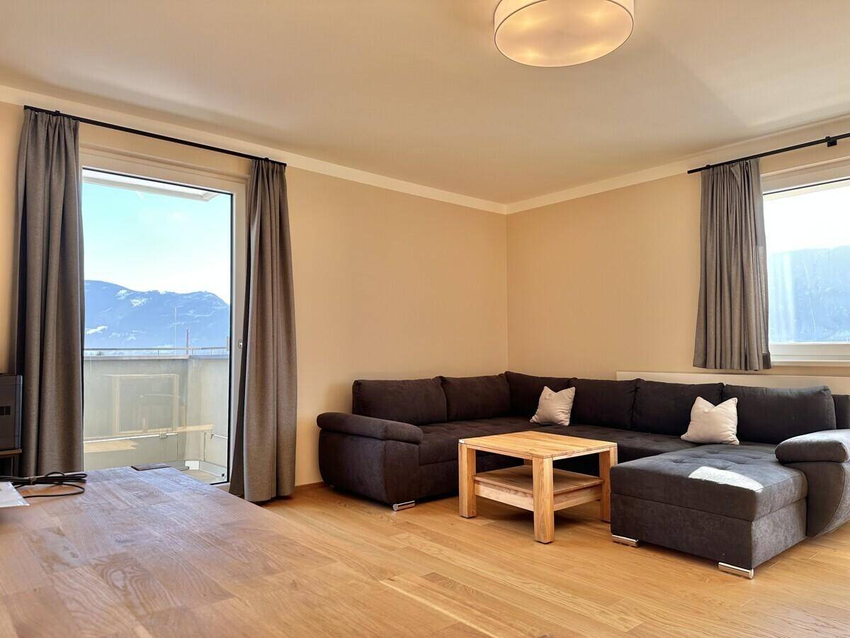 Geräumiges Wohnzimmer mit dunklem Sofa, Holztisch und Balkonzugang.