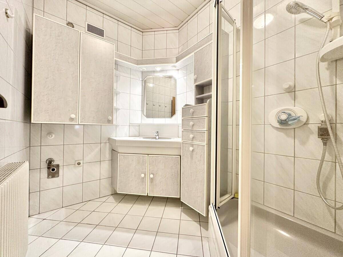 Helles Badezimmer mit weißen Fliesen, Dusche und integriertem Waschtischunterschrank.
