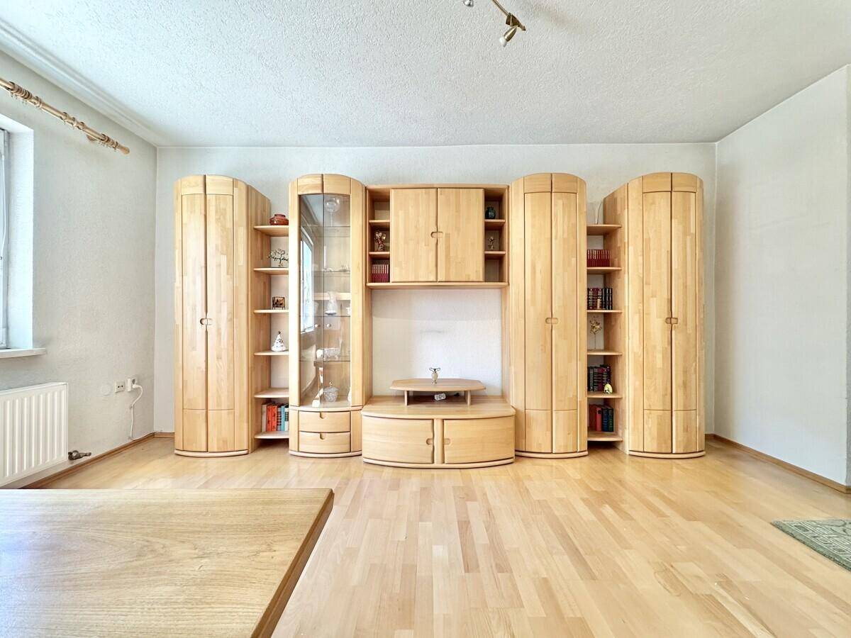 Geräumiges Wohnzimmer mit Parkettboden und einer großen Holzschrankwand.