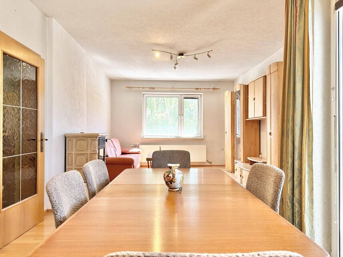 Heller Wohn- und Essbereich mit Holztisch, Parkettboden und Blick ins Grüne.
