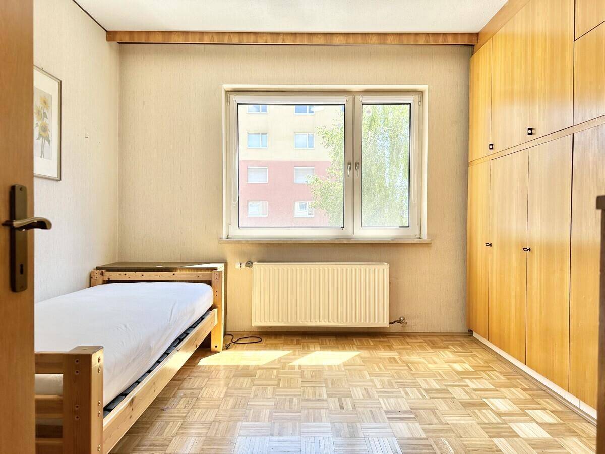 Schlafzimmer mit Parkettboden, Einzelbett und großem Fenster mit Blick auf die Umgebung.