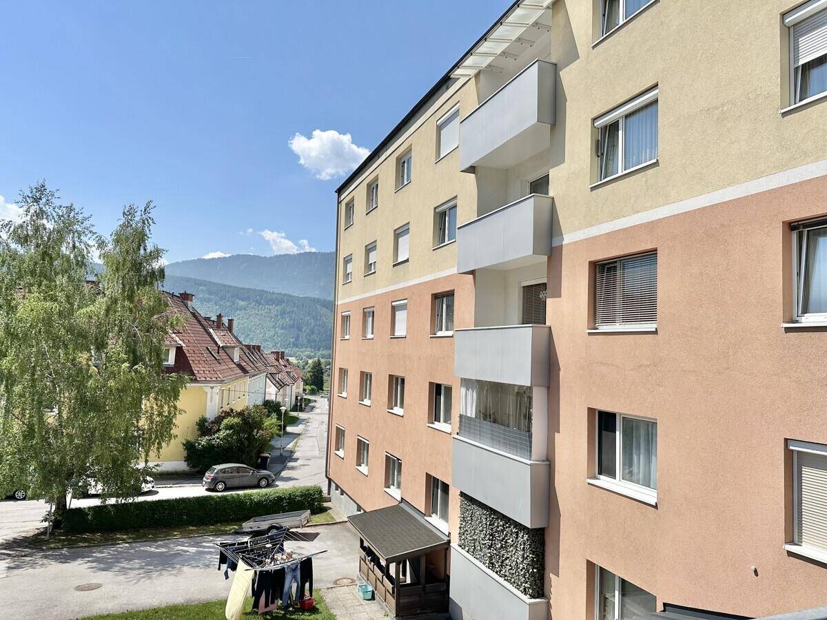 Seitenansicht des Mehrfamilienhauses mit Balkonen und Blick auf die Berge.