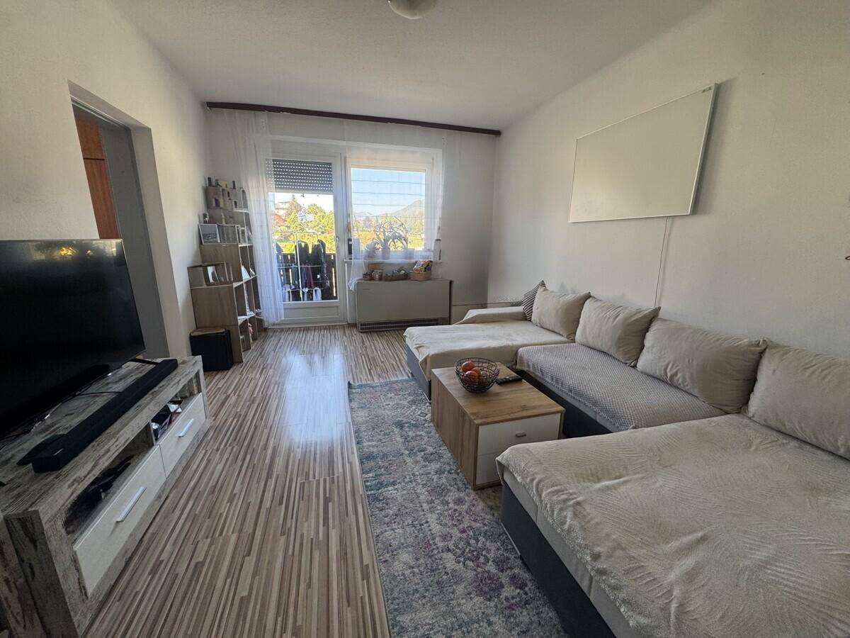 Helles Wohnzimmer mit großem Ecksofa, Laminatboden und Zugang zum Balkon.