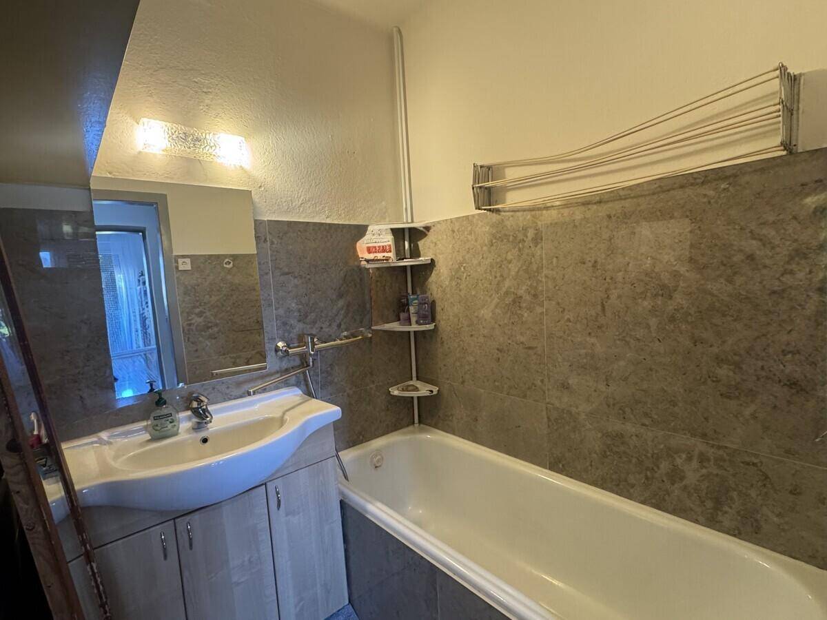 Badezimmer mit Badewanne, Einzelwaschbecken und teilweise gefliesten Wänden im 80er-Jahre-Stil.