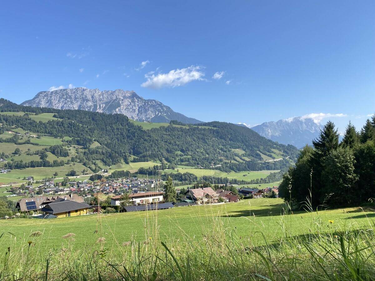 Panoramablick über ein Tal mit Dorf, grünen Feldern und majestätischen Bergen.