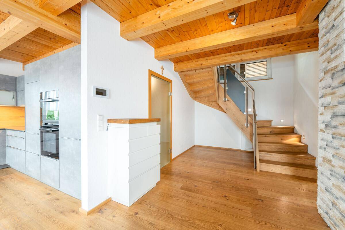 Übergangsbereich von der Küche zum Flur mit offener Holztreppe und sichtbaren Holzbalken.