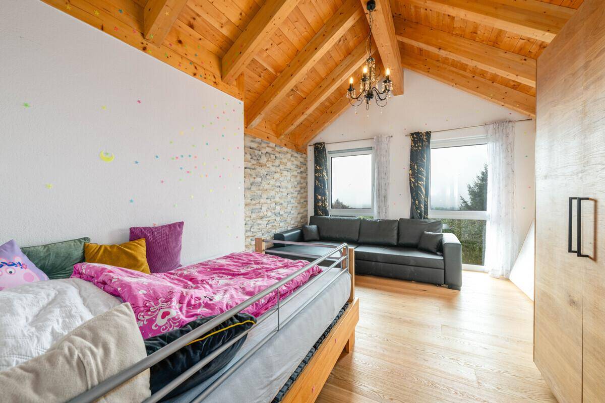 Geräumiges Schlafzimmer im Dachgeschoss mit Holzbalkendecke, Steinwand und Sitzbereich.