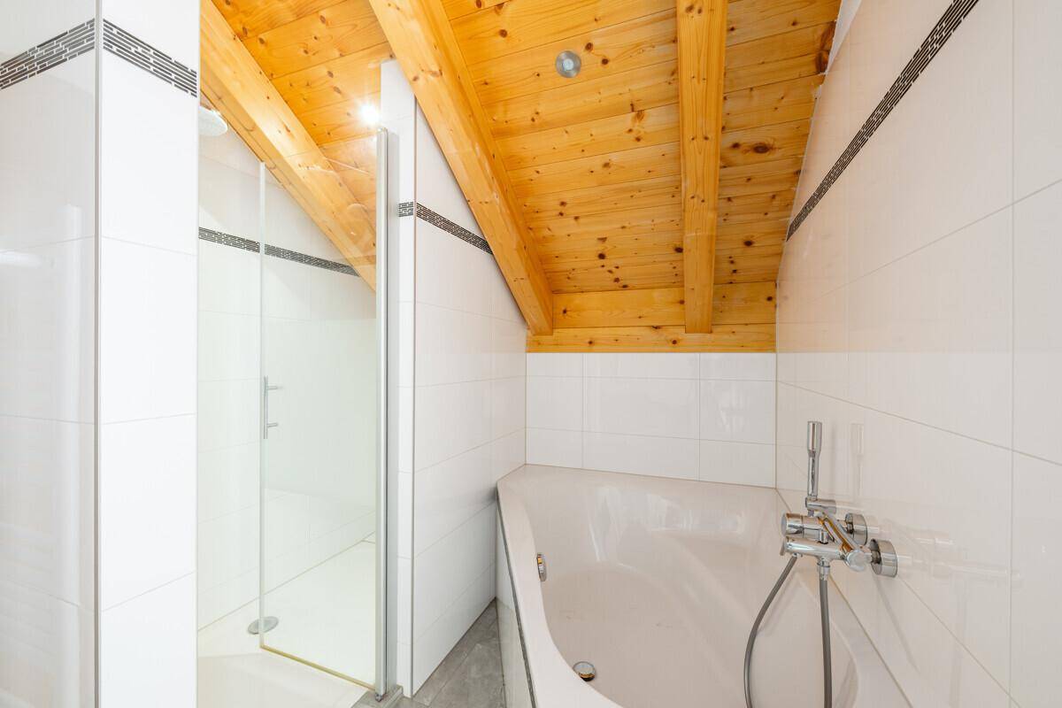 Modernes Badezimmer im Dachgeschoss mit Dusche, Eckbadewanne und Holzbalkendecke.