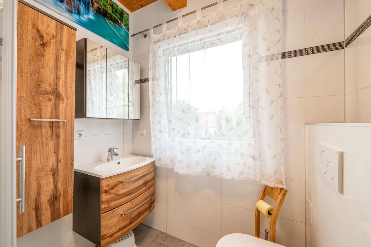 Kleines Badezimmer mit Waschbecken, Toilette und Fenster, hell gefliest und funktional eingerichtet.