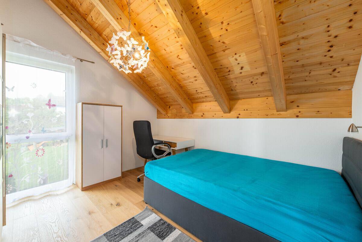 Helles Schlafzimmer im Dachgeschoss mit Holzbalkendecke, Einzelbett und Schreibtisch.